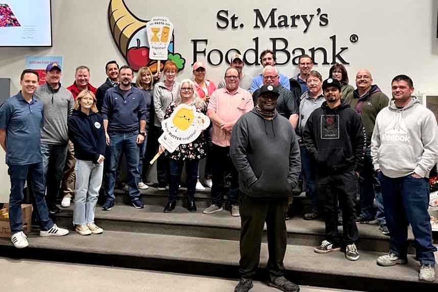 Group of volunteers at St. Mary's Food Bank, smiling, holding food donation signs