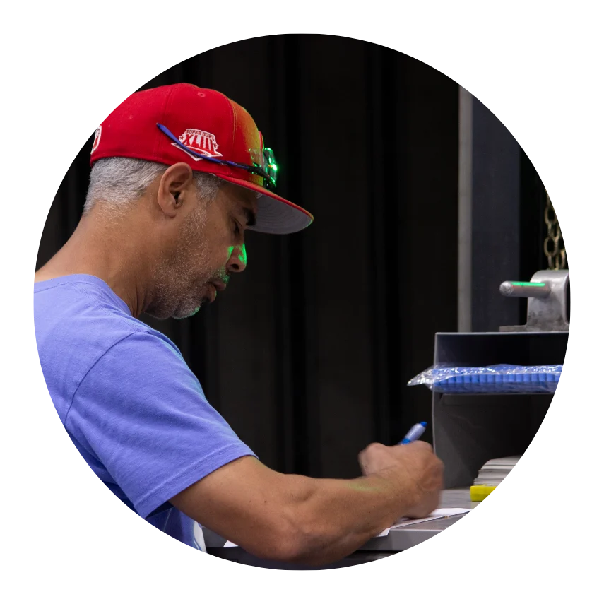 Man in a red cap and blue shirt writing with a pen at a workstation table