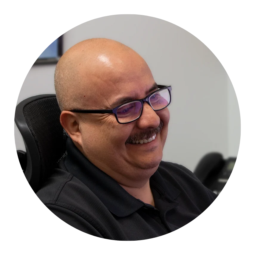 Smiling man wearing glasses in an office setting, seated on an ergonomic chair