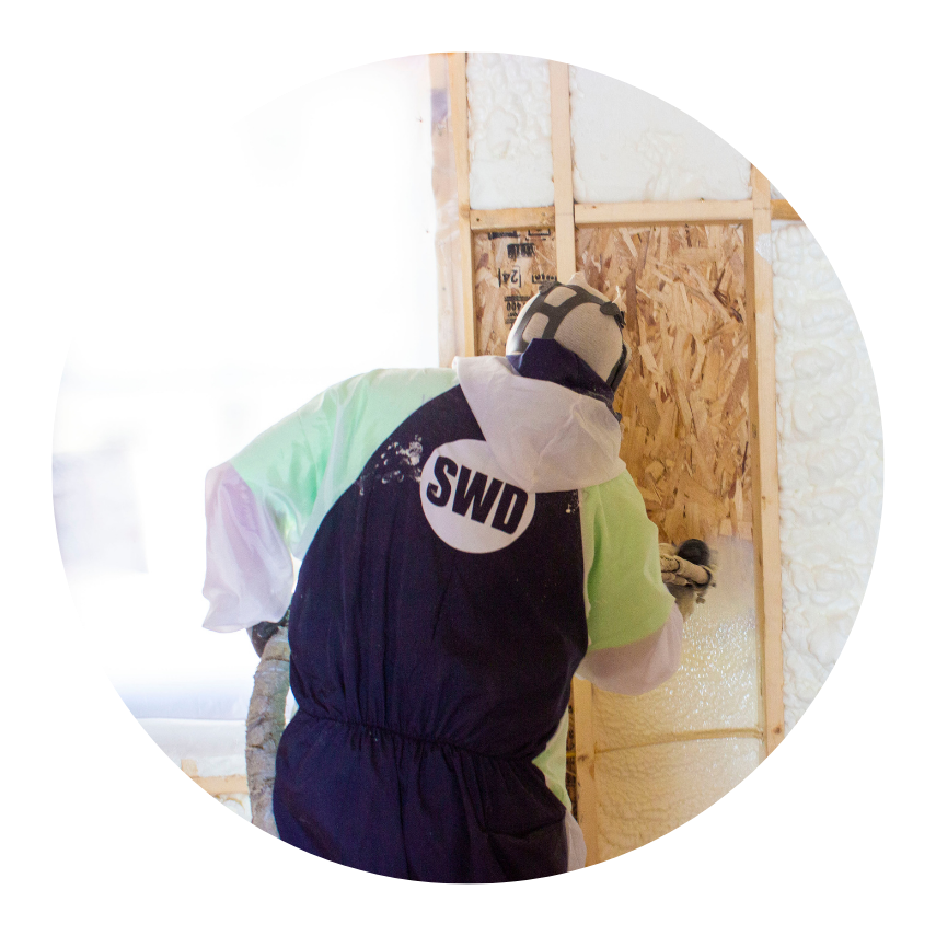 Installer applying open-cell spray foam insulation between wall studs inside a residential construction site.