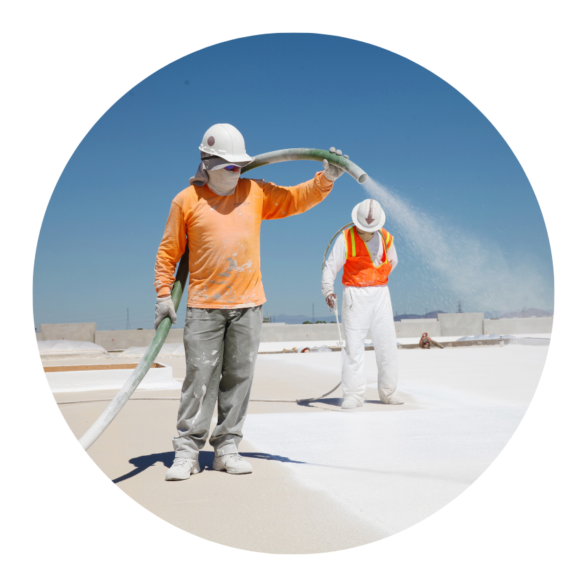 Construction worker in safety gear spraying spray foam roofing insulation on a flat roof under a clear blue sky.