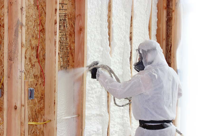 A spray foam insulation installer uses a hose to apply foam to exposed wall framing at an SWD Urethane job site.